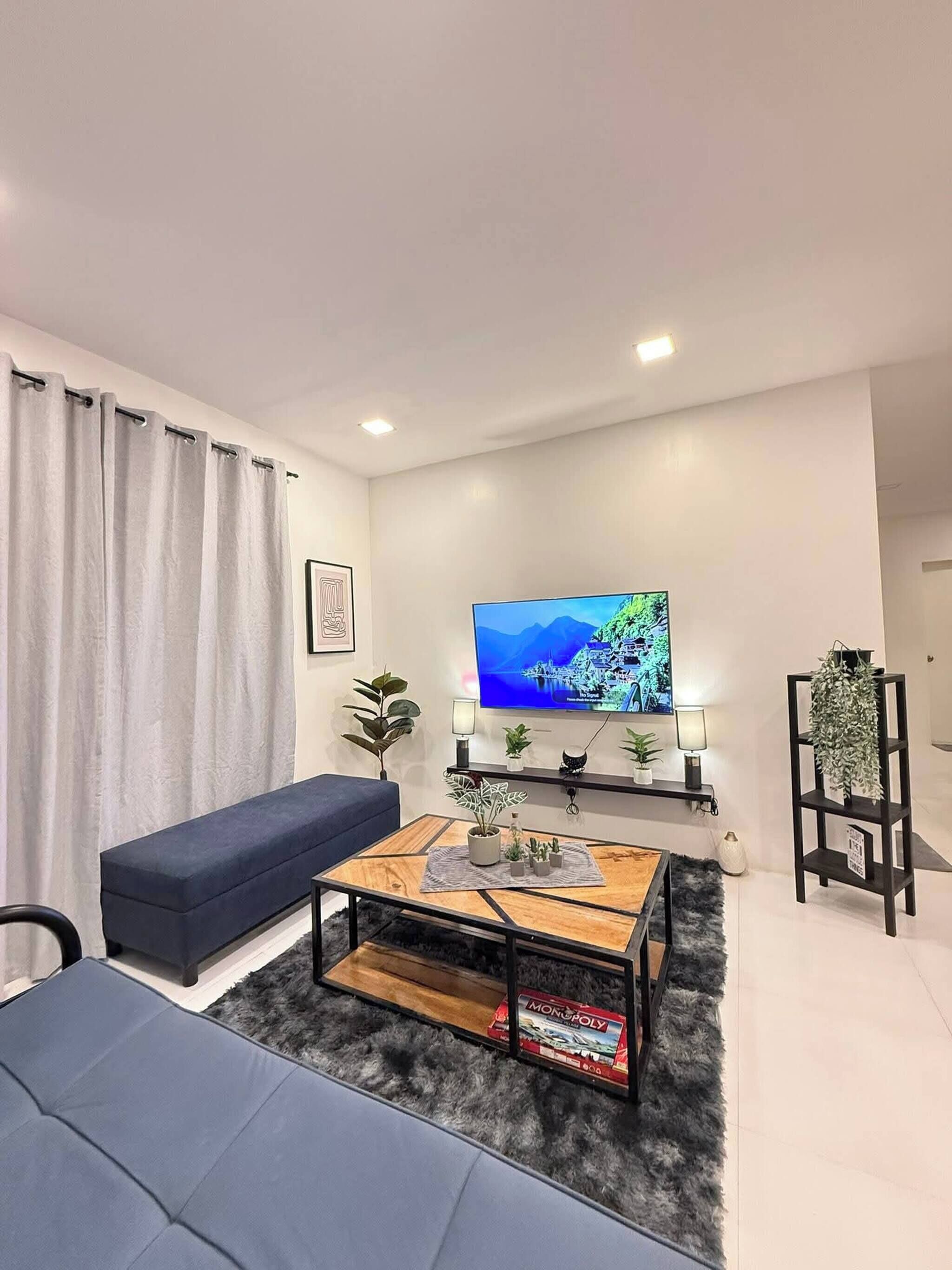 Una sala de estar moderna con un sofá, una mesa de centro con plantas, un televisor en la pared y un pequeño estante con adornos.