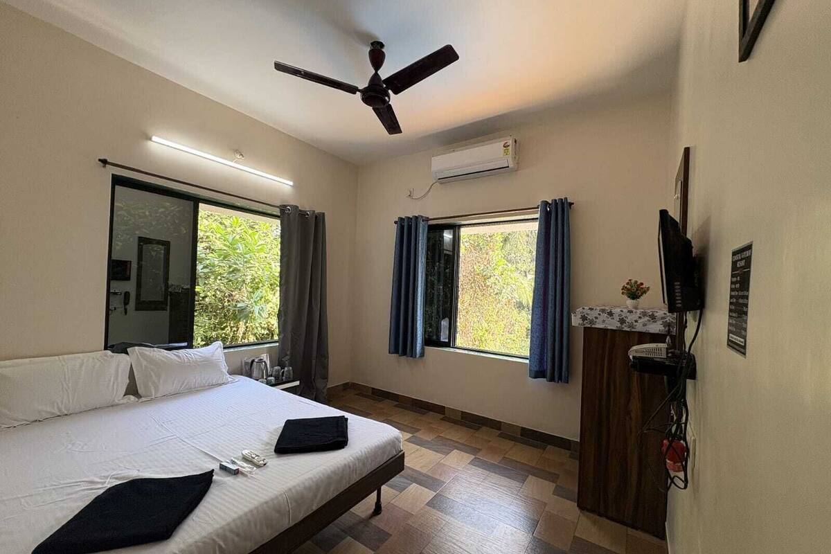 A bedroom with a bed, a ceiling fan, a window with curtains, an air conditioning unit, and a television on a stand.