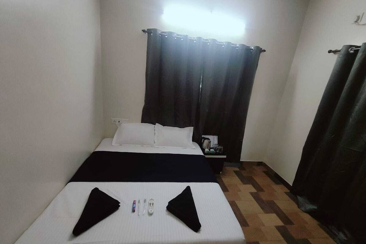 A small, simple room with a bed, a nightstand, and a window with curtains.