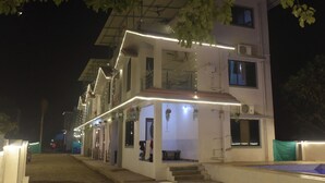 Un edificio de varios pisos con un balcón, un espacio exterior cubierto y plantas colgantes.