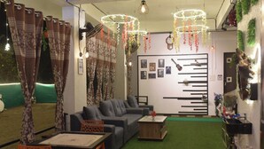Un salón acogedor con sofá, sillones, una mesa de centro y una mesita con un jarrón. Se observan cortinas, un reloj y una pared adornada con cuadros.