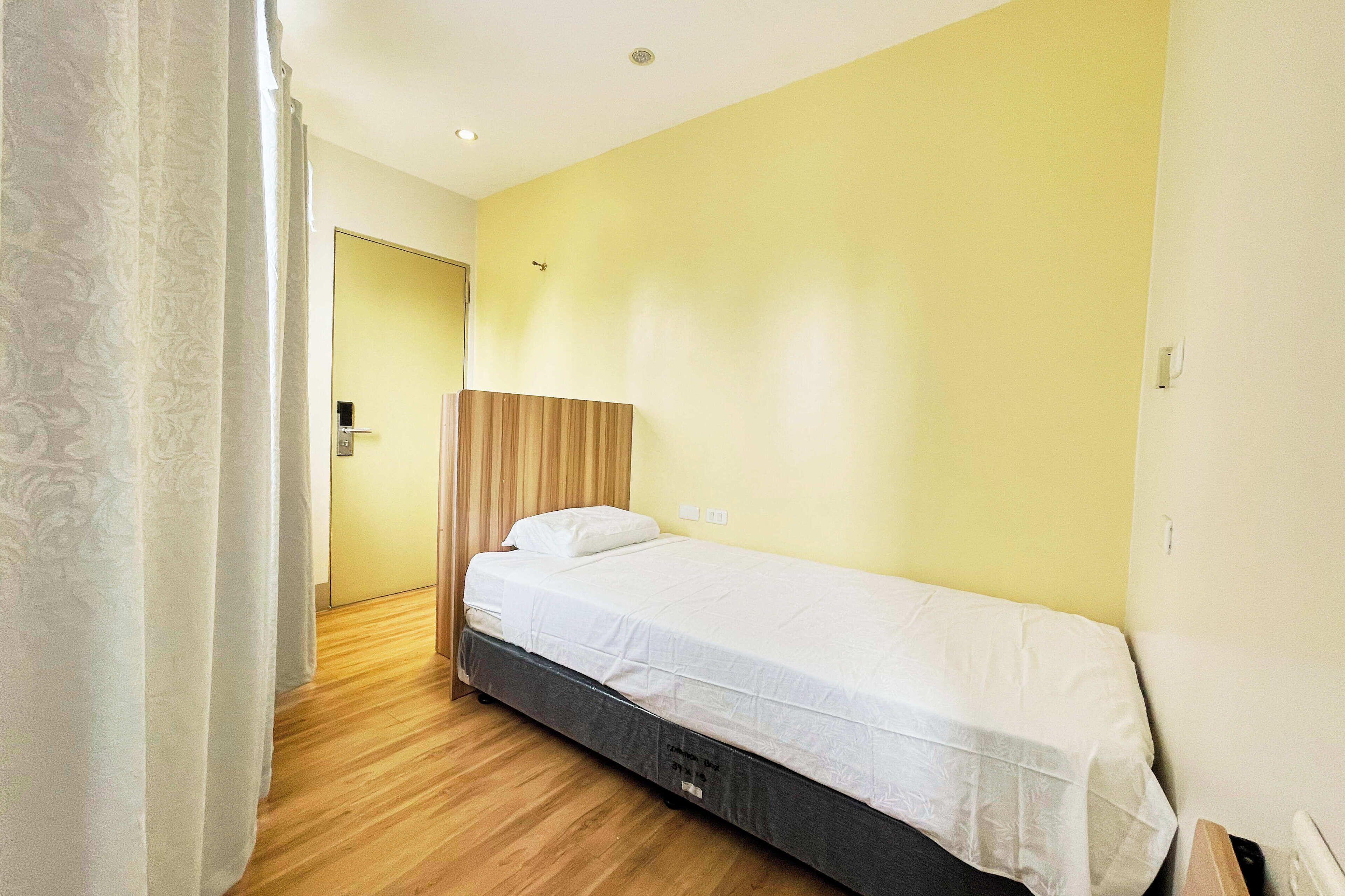 A single bed with a wooden headboard, a white mattress, and a wooden floor.