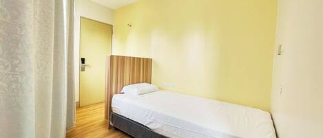 A single bed with a wooden headboard, a white mattress, and a wooden floor.
