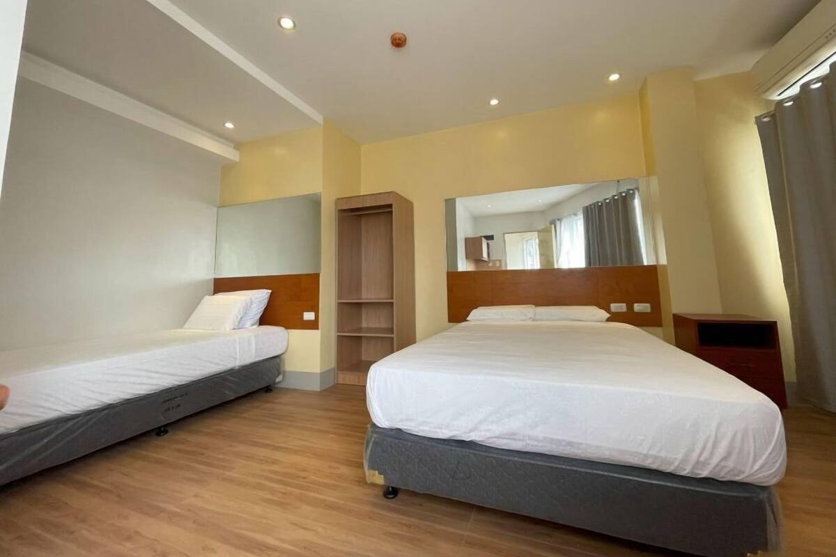 A hotel room with two single beds, a wooden wardrobe, a mirror, and a small bedside table.