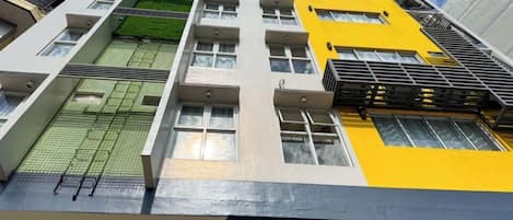 A multi-story building with a modern architectural design, featuring balconies, large windows, and a mix of white and yellow facades.
