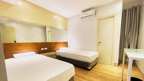 Ein Hotelzimmer mit zwei Einzelbetten, einem hölzernen Kopfteil, einem weißen Schreibtisch, einem Spiegel und einer Klimaanlage.