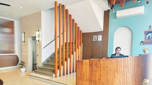 A reception area with a wooden staircase, a reception desk, and a wall-mounted air conditioner. - Hotel Casa Del Sol (Raipur)