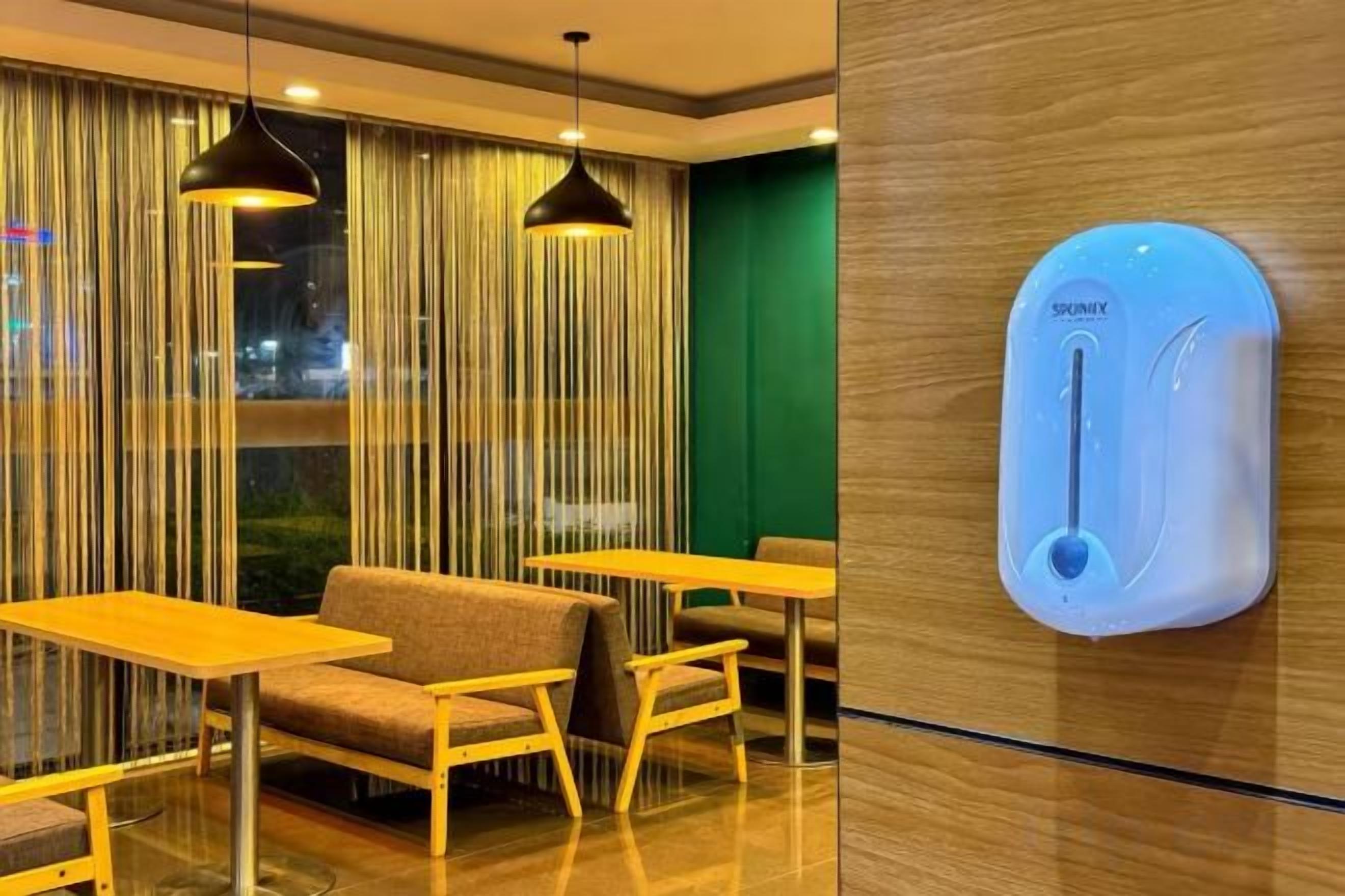 A hotel room with a sofa, tables, and a wall-mounted hand sanitizer dispenser.