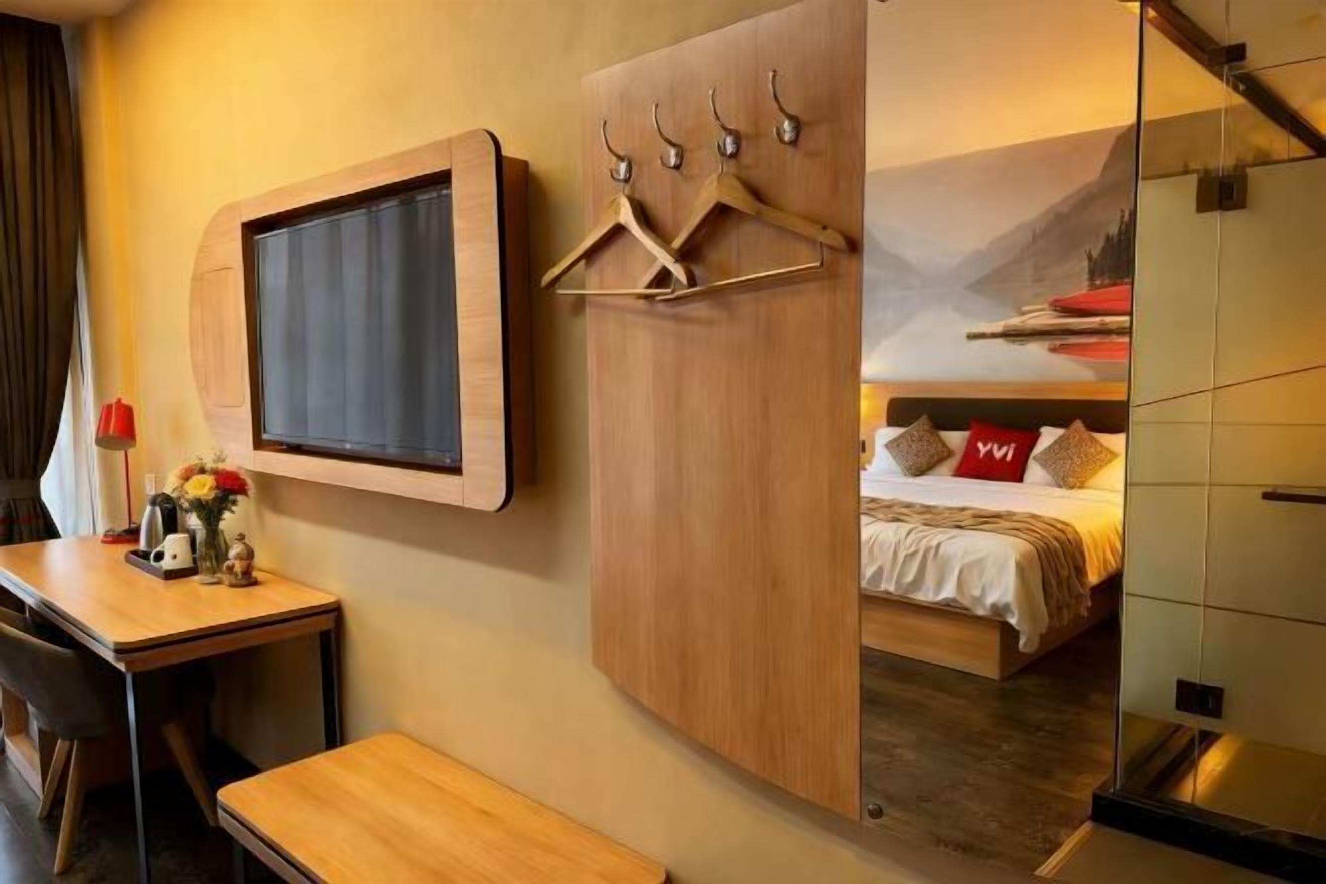 Une chambre d’hôtel avec un lit, un bureau, une chaise, un porte-manteau et une grande fenêtre.