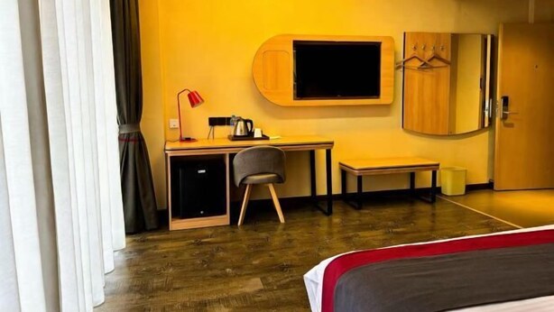 A hotel room with a wooden desk, a television mounted on the wall, a bed, a chair, and a wardrobe. - Taishan guest house (Addis Ababa)