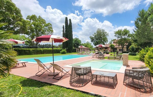 Piscina com espreguiçadeiras e guarda-sóis, rodeada por vegetação e um céu claro.