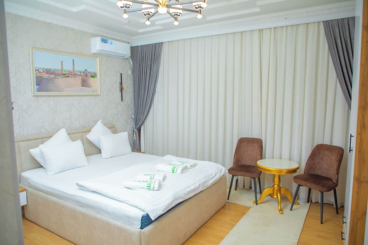 A hotel room with a large bed, two chairs, a small round table, and a painting on the wall.