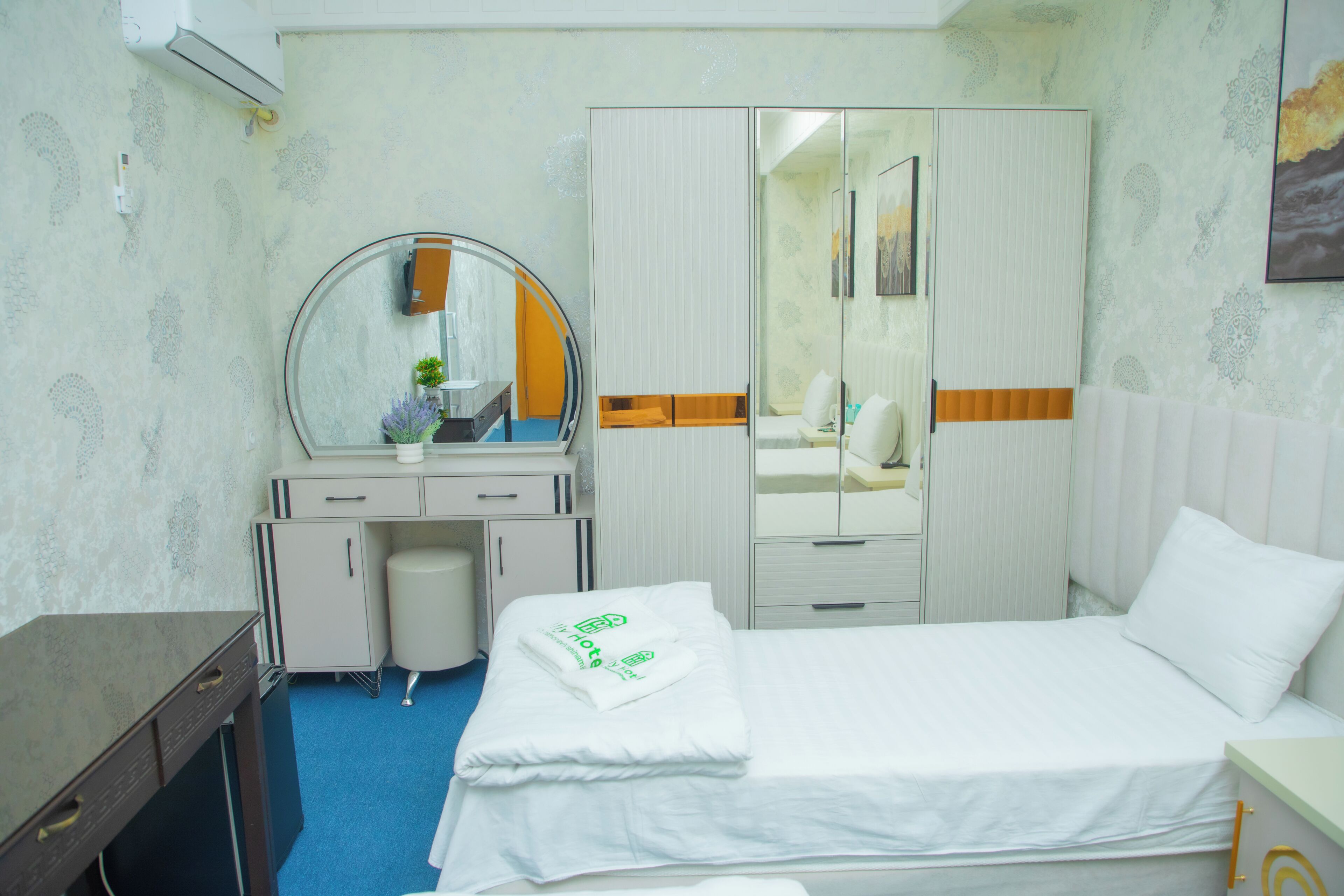 A hotel room with a bed, a desk with a mirror, a wardrobe, and a bathroom.