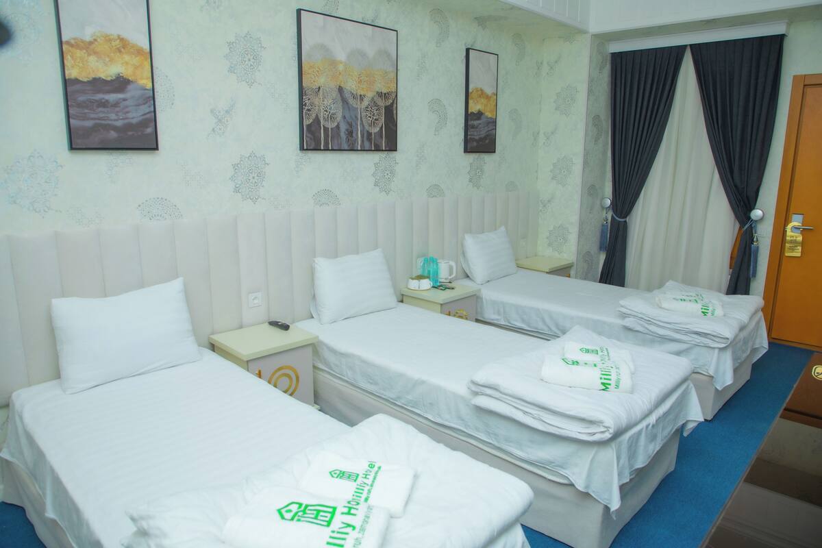 A hotel room with two beds, a nightstand, a wall clock, and two paintings.