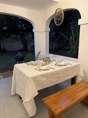 Comedor con una mesa dispuesta para cuatro personas, rodeado de paredes blancas y vistas al jardín.