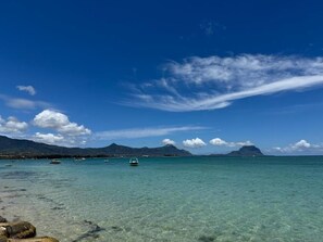 A clear blue sea with boats, rocky shore, and mountains in the background. - Martello Duplex - 1 Min Walk to La Preneuse Blue Sea (La Preneuse)