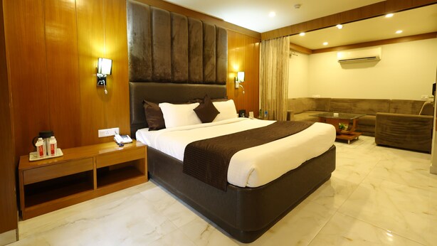 A hotel room with a large bed, wooden paneling, a sofa, and a small table. - Hotel Metro Agra (Agra)