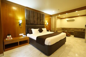 A hotel room with a large bed, wooden paneling, a sofa, and a small table. - Hotel Metro Agra (Agra)