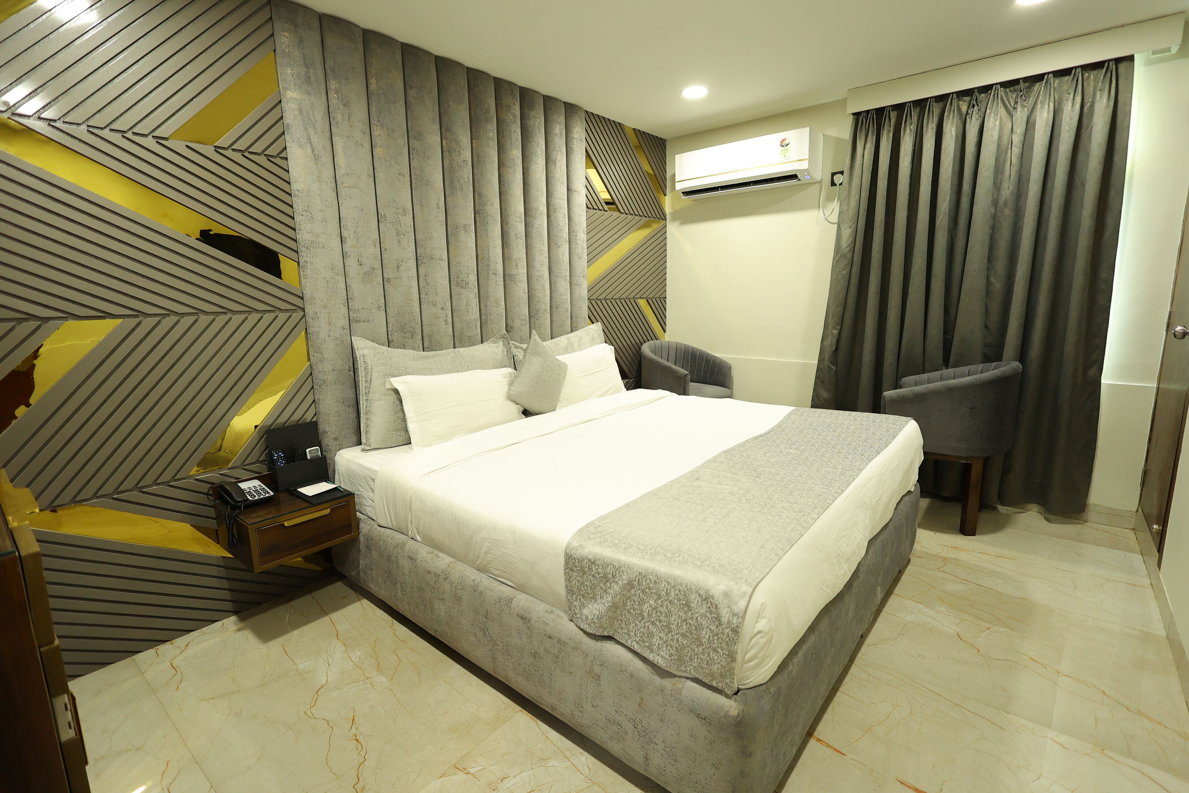 Een moderne hotelkamer met een groot bed, een nachtkastje met een telefoon, en een stoel.