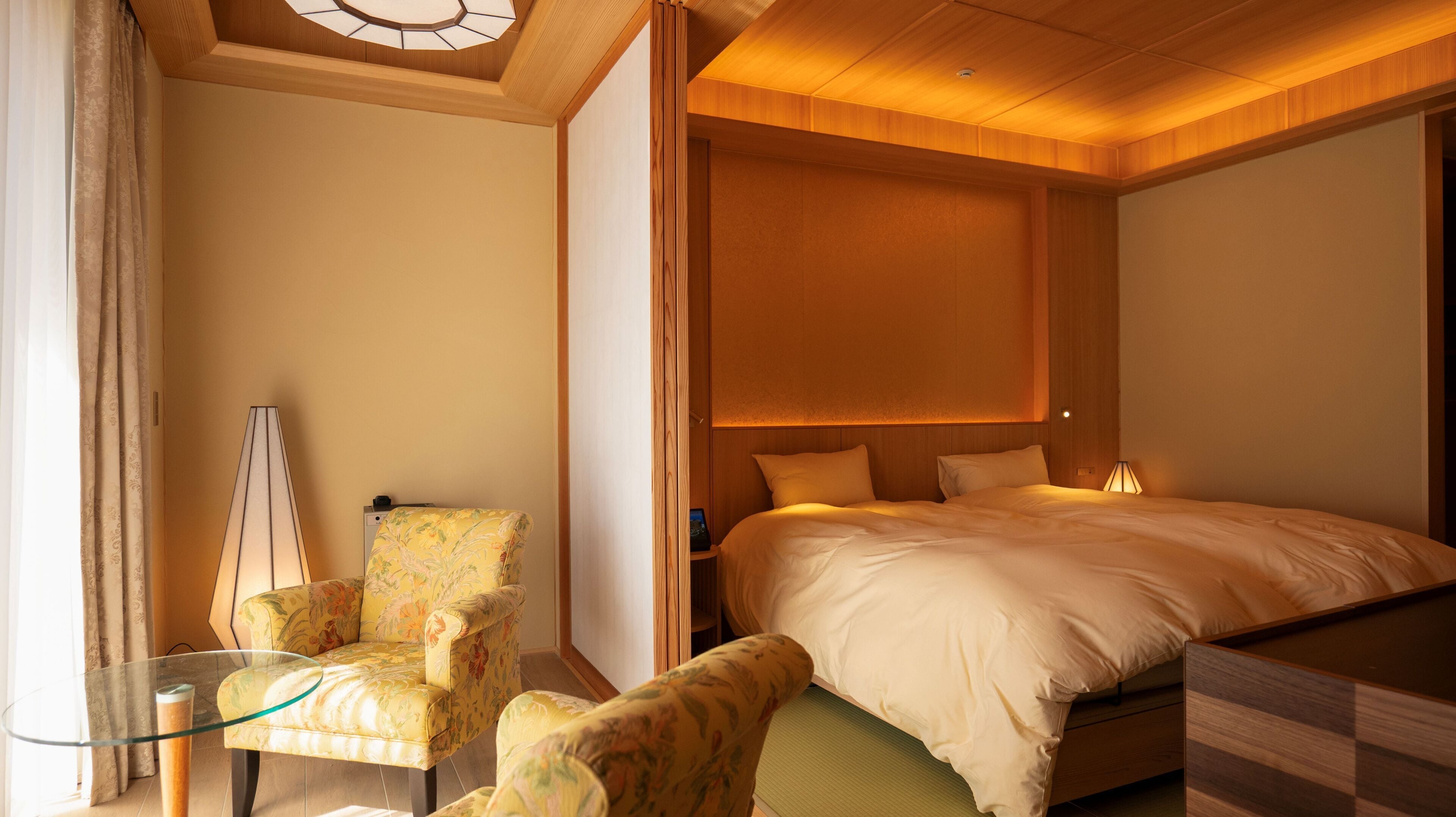 A hotel room with a bed, a chair, a table, and a ceiling light fixture.