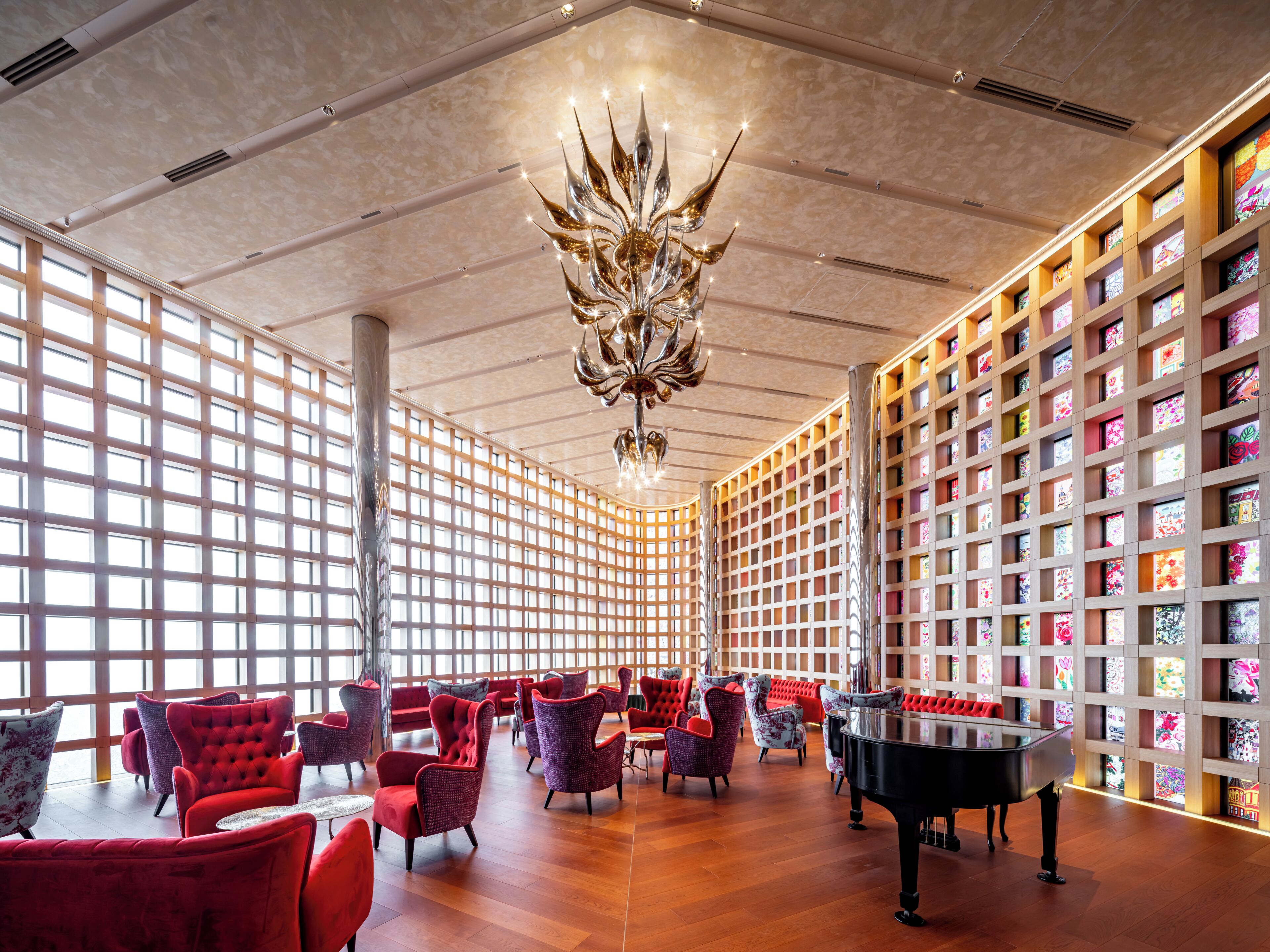 A spacious room with a grand piano, red upholstered chairs, and a unique chandelier.