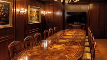 A conference room with a long wooden table, chairs, a chandelier, a painting, and a television.