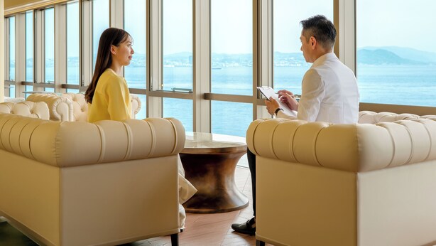A room with two sofas facing each other, a coffee table, and large windows with a view of the sea and distant land. - THE PASONA natureverse retreat (Awaji)