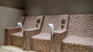 A row of three shower stalls with tiled walls and benches, equipped with handheld shower heads.