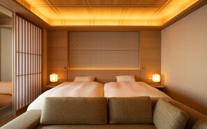 A hotel room with a large bed, two bedside lamps, a wooden headboard, and a futon with cushions. - THE PASONA natureverse retreat (Awaji)