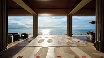 A spacious indoor area with a view of the sea, featuring a pool with lounge chairs and a bar area.