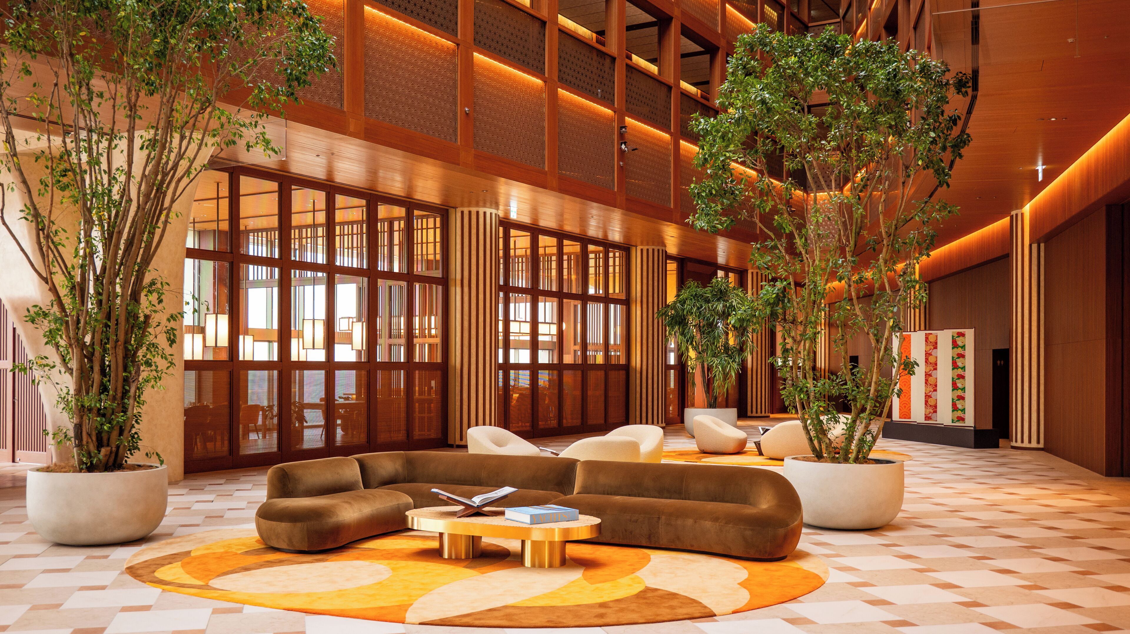 A modern lobby with a sectional sofa, a coffee table, and large potted plants.
