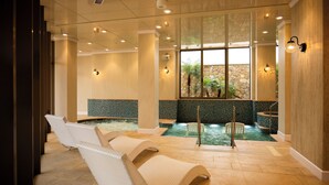 A spa area with a hot tub, lounge chairs, and a stone wall with a view of greenery. - THE PASONA natureverse retreat (Awaji)