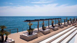 A seaside promenade with a wooden pergola, palm trees, and a view of the ocean. - THE PASONA natureverse retreat (Awaji)