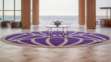 A spacious room with a large view of the ocean, a round table with a decorative centerpiece, and a purple patterned rug.