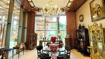 A spacious room with a chandelier, ornate furniture, and large windows offering a view of greenery.