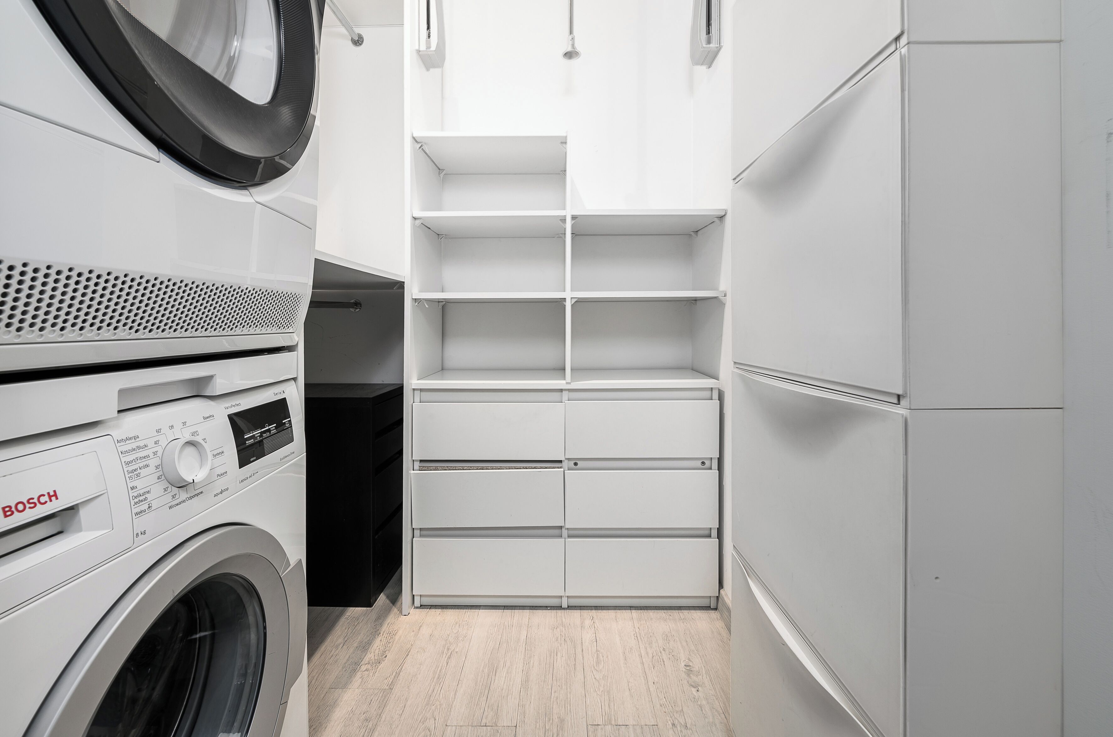 A compact laundry room with a Bosch washing machine, a built-in drying rack, and a white shelving unit.