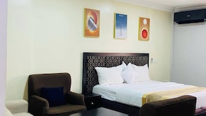 A hotel room with a bed, two armchairs, a small table, and three wall art pieces. - Sienna Suites (Abuja)
