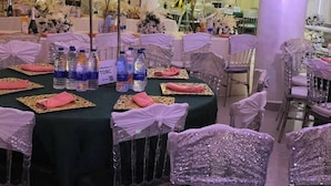A banquet hall with round tables covered in green tablecloths, adorned with pink napkins and clear plastic water bottles. - Sienna Suites (Abuja)