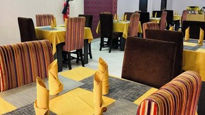 A dining area with tables and chairs, some with yellow tablecloths and striped cushions. - Sienna Suites (Abuja)