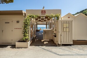 Ein Gebäude direkt am Strand mit überdachter Eingang, einem sichtbaren Restaurant namens 'IL RISTORANTE' und freiem Blick auf das Meer.