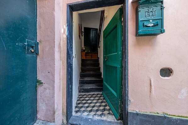 Un escalier menant à une pièce dotée d’une porte verte, d’une boîte aux lettres et d’un sol carrelé.