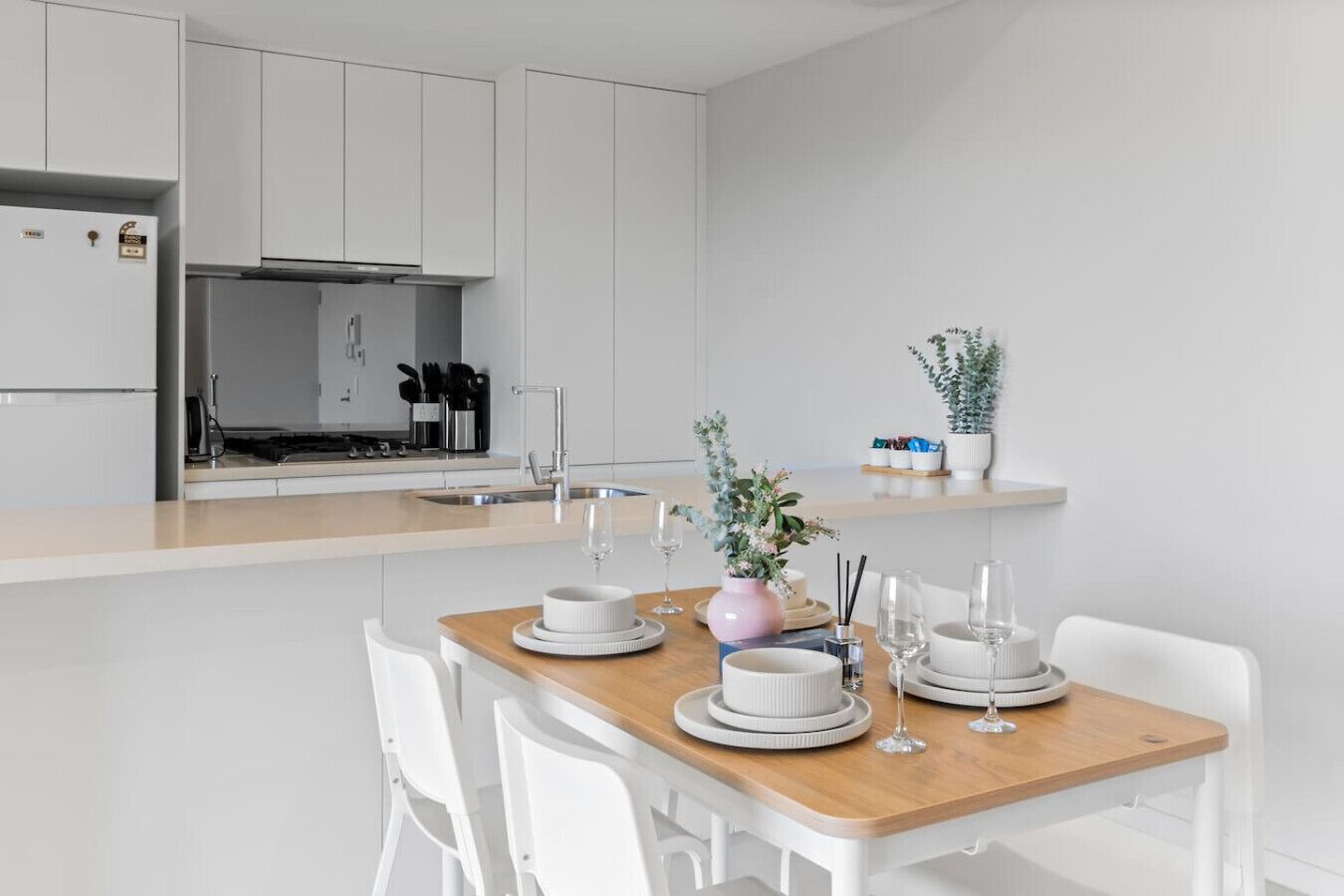 A modern kitchen with white cabinets, a wooden dining table, and a small island with a sink.