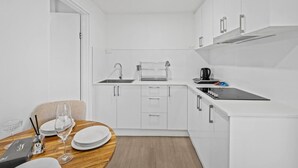 Een kleine keuken met witte kastjes, een spoelbak en een aanrecht. Er staat een eettafel met borden en glazen.