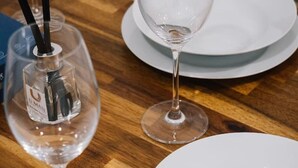 Een houten tafel met drie witte borden en twee wijnglazen, waarvan één een zwart rietje heeft.