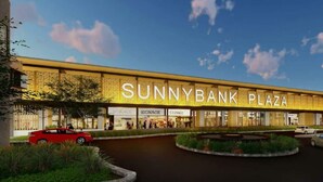 Een modern gebouw met het bord "SUNNYBANK PLAZA" en verschillende winkelgefaciliteiten met de aanduiding "SIGNAGE".
