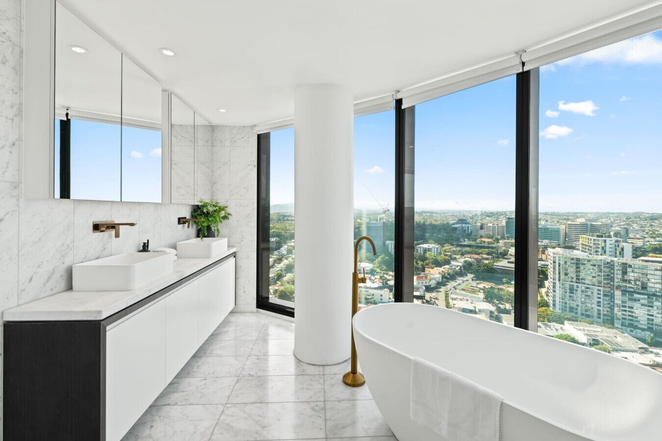 Une salle de bain moderne dotée d’une grande baignoire, d’un meuble-lavabo avec un miroir et offrant une vue sur le paysage urbain grâce à de grandes fenêtres.