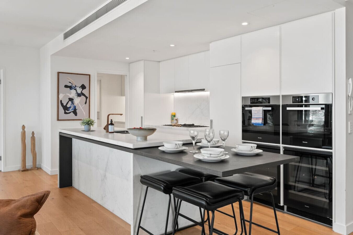 Una cocina moderna con armarios blancos, encimera de mármol y taburetes negros.