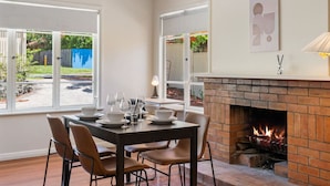 Un comedor con chimenea de ladrillo, una mesa preparada para cuatro personas y ventanas amplias con vistas al exterior.
