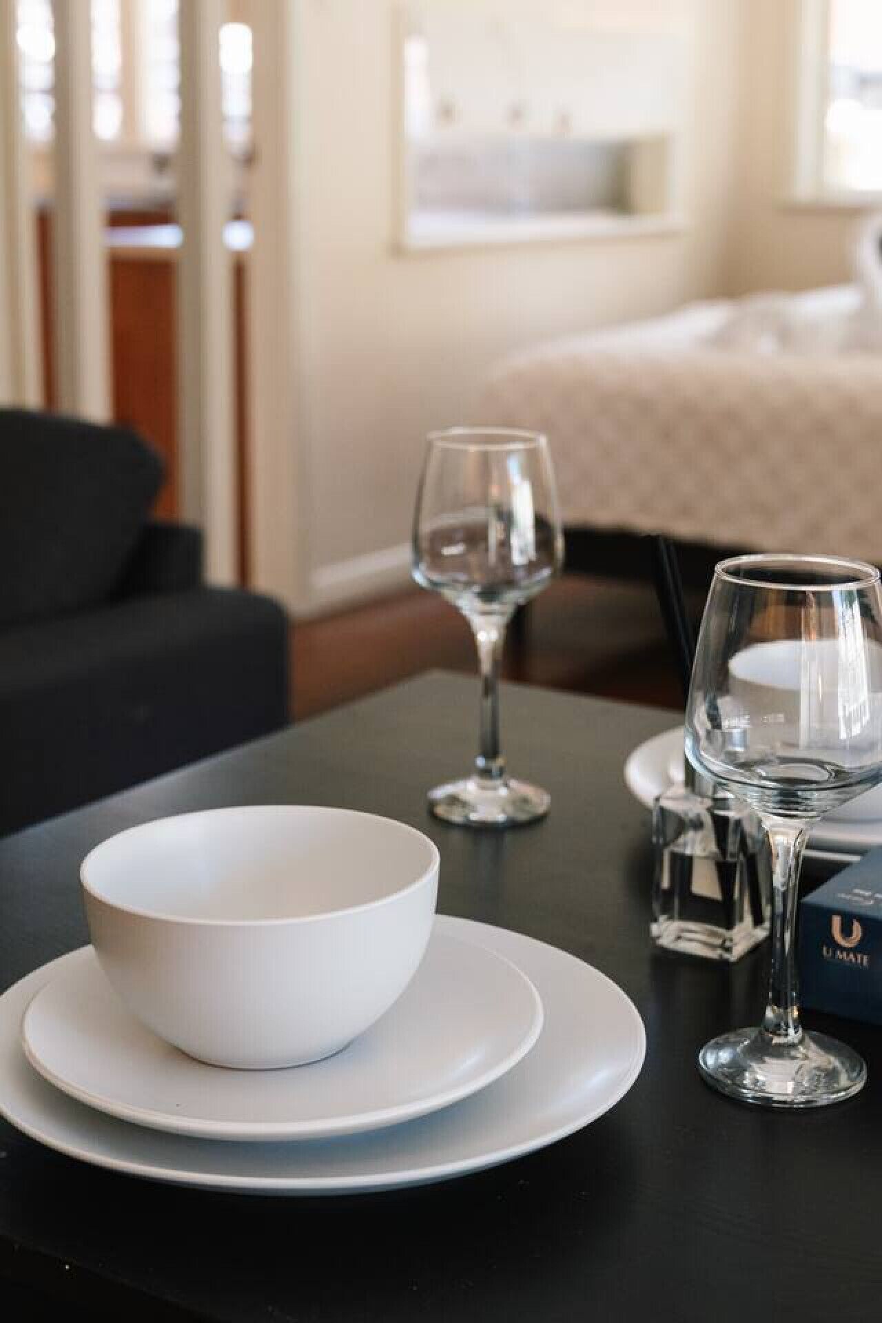 A dining table with a white bowl and plates, two wine glasses, and a box labeled "U MATE".