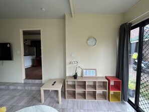 A living room with a TV, a wooden table, a potted orchid, a clock, and a window with curtains. - Cozy 1BR Flat in Sunnybank | Solo&Couple Travelers (Sunnybank)